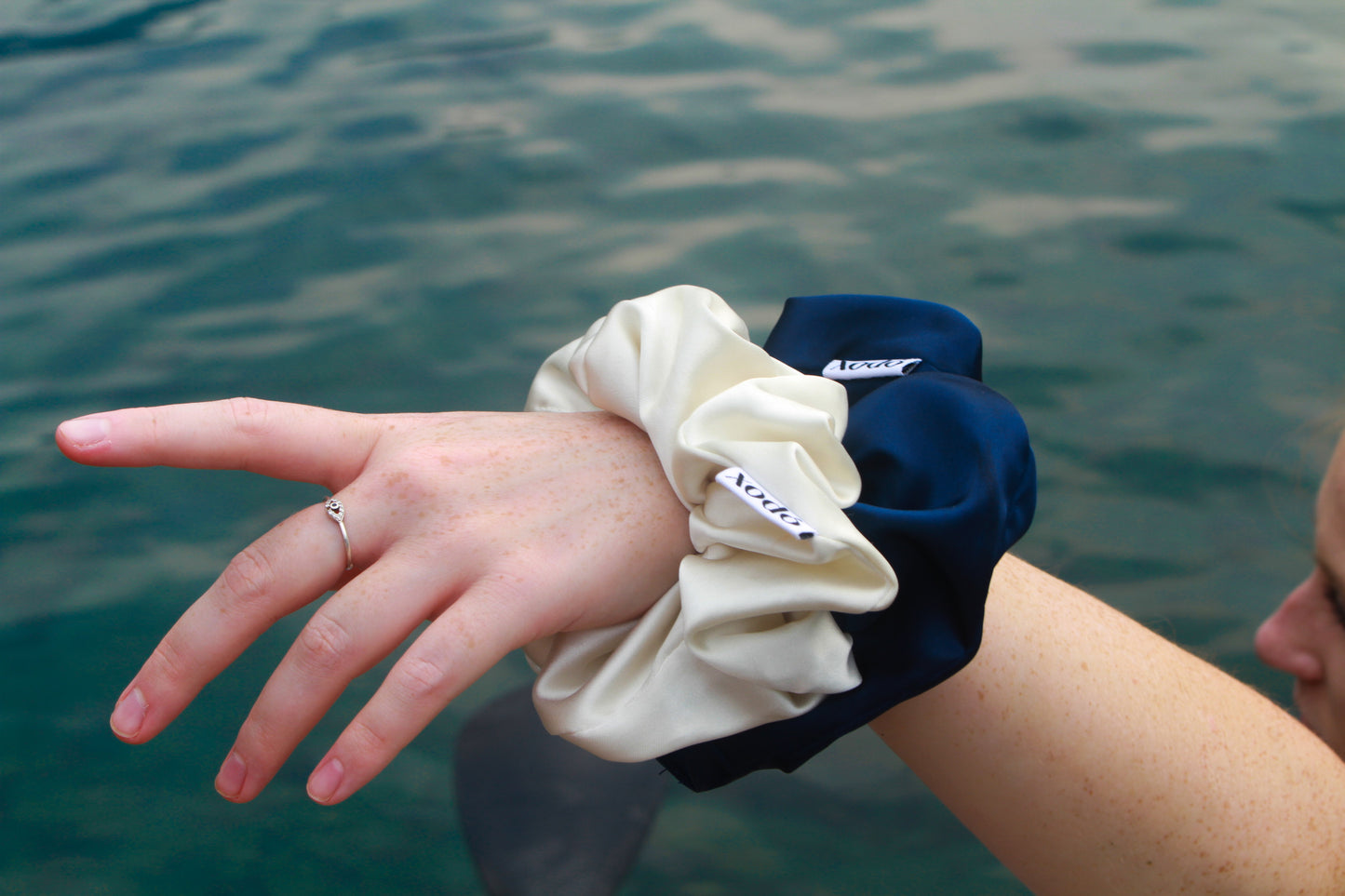 Two scrunchies, one white and one navy, on a wrist with water in the background