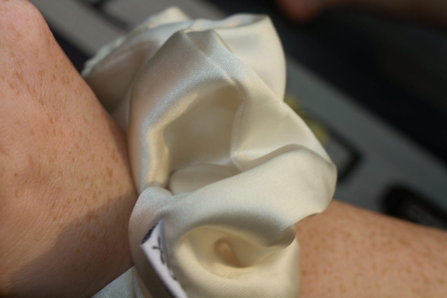 Close-up of a wrist wearing a white scrunchy with a blurred background